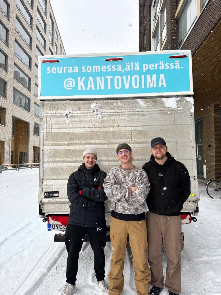 Kantovoiman tiimi poseeraa muuttoauton edessä talvella