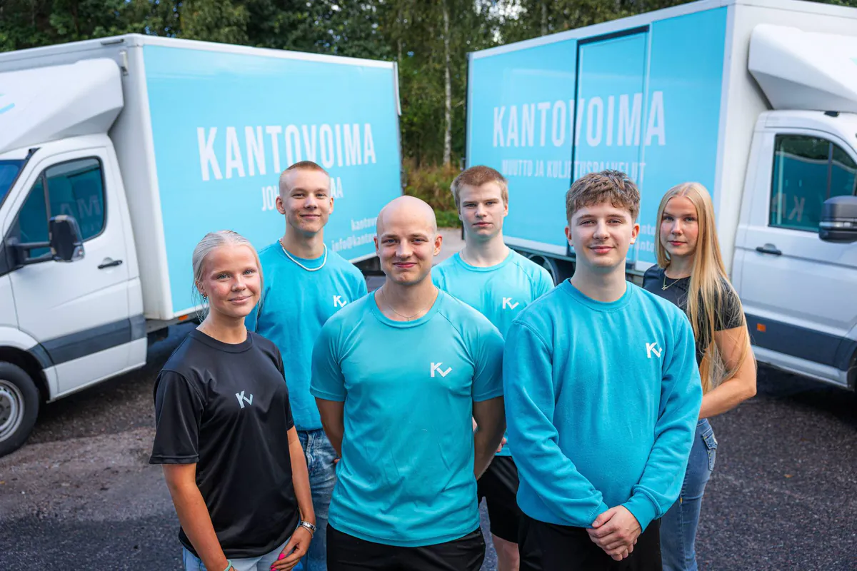 Kantovoiman kuusihenkinen tiimi seisoo kahden turkoosin muuttoauton edessä