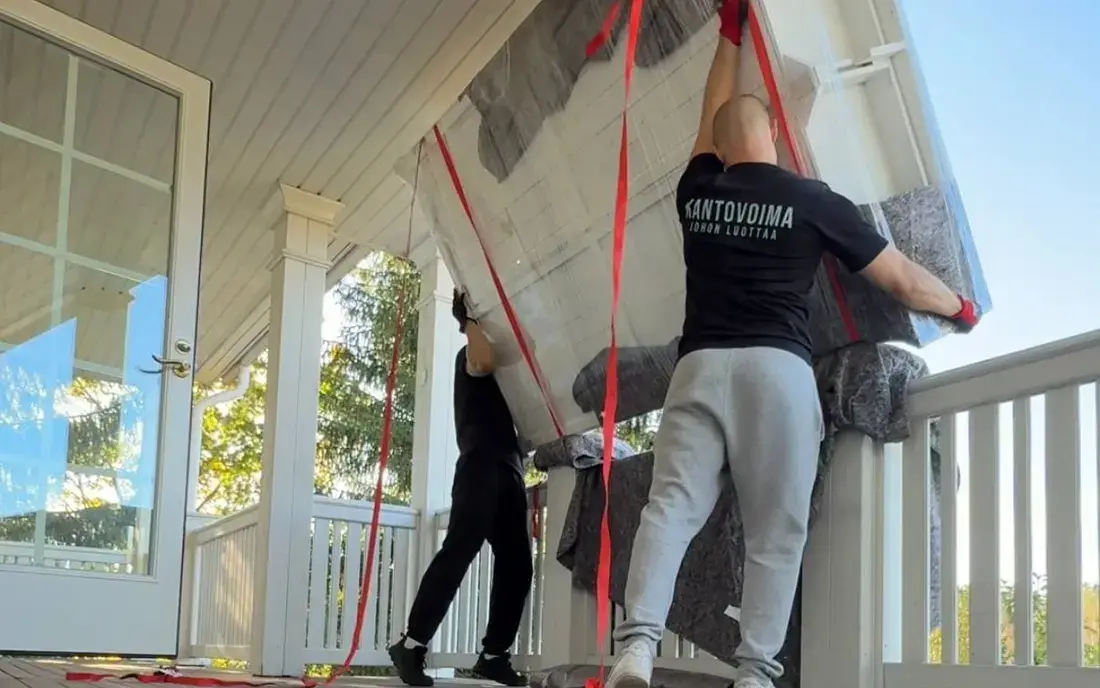 Two Kantovoima movers carrying a blanket-wrapped item with lifting straps